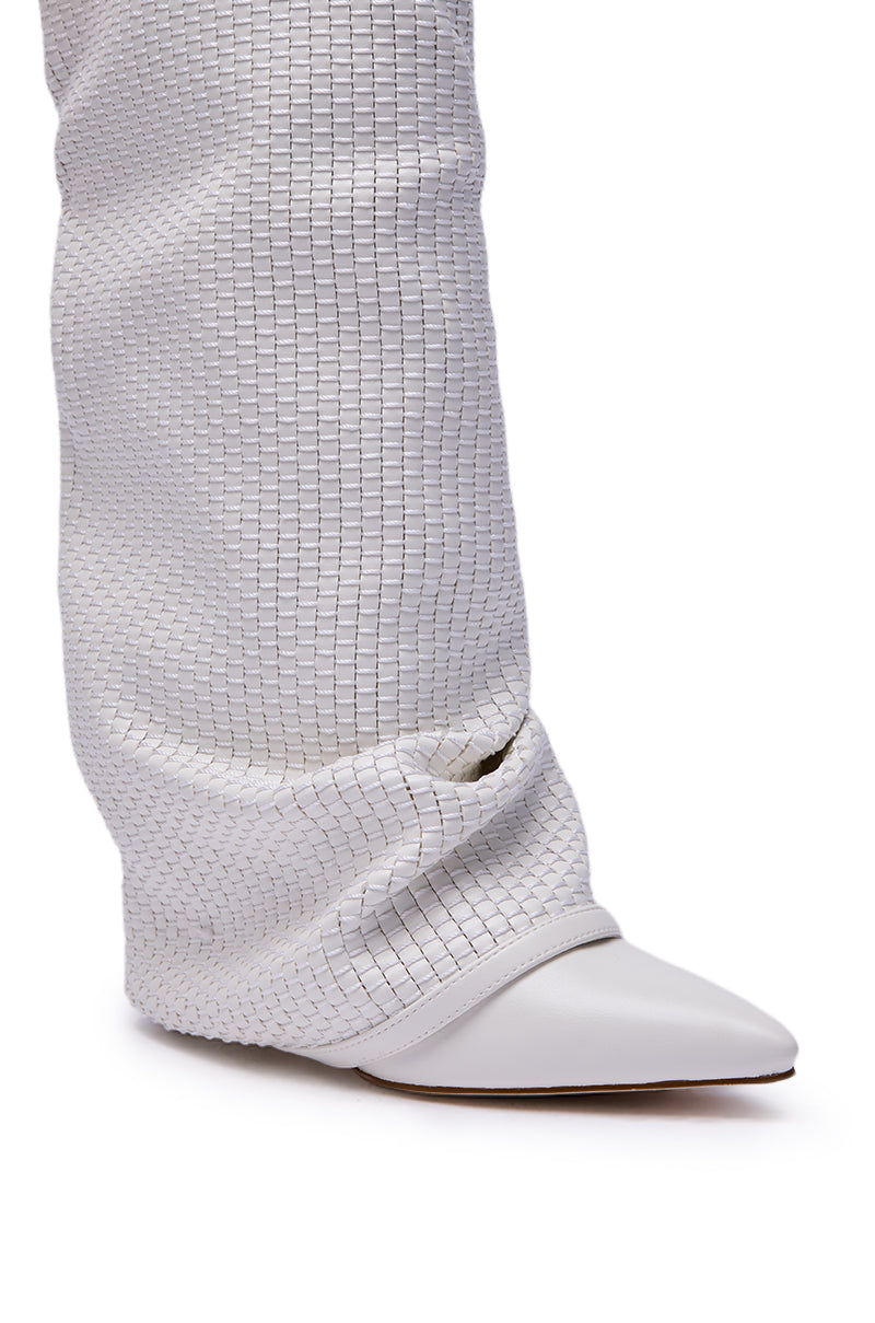 A close-up of a leg in wide, textured white pants draped over the AZALEA WANG BRETANGE Woven PU Fold Over Boot in White, with the pant hem slightly gathered near the pointed knee-high boot. 8