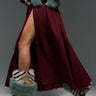 A person walks with a burgundy skirt featuring a high slit, paired with the AZALEA WANG BRIENNE MULTI BOOTIE and a fur-trimmed coat. The fur showcases a mix of teal and natural stripes, adding a bold contrast to the outfit.