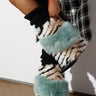 An individual in the chic AZALEA WANG BRIENNE MULTI BOOTIE, showcasing striped and turquoise fur accents along with a blocky wedge heel, matched perfectly with a black and white plaid coat. The boots present a unique design with plush textures, creating an interesting contrast against the sleek pattern of the coat.