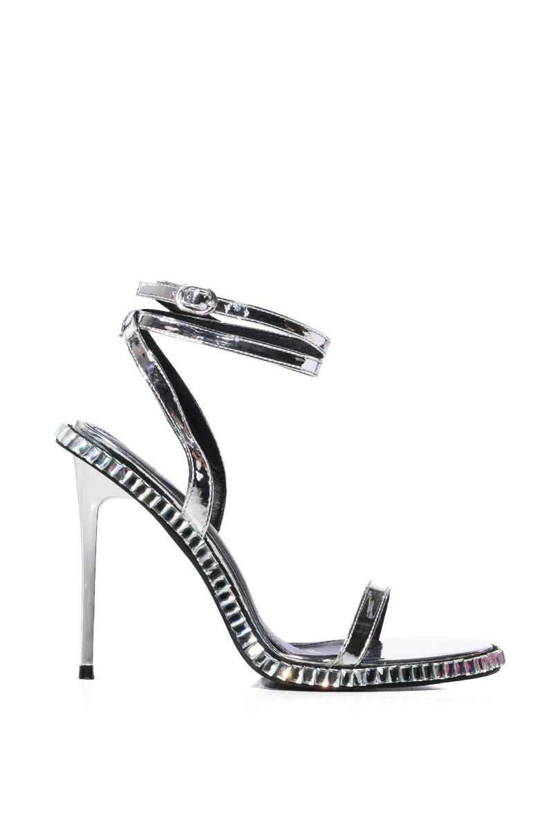 The AZALEA WANG BRIK black stiletto sandal with silver features iridescent details, a rhinestone trim, a thin heel, an ankle strap with buckle, and a single toe strap. Its glossy faux leather finish is enhanced by decorative metallic edging along the sole.