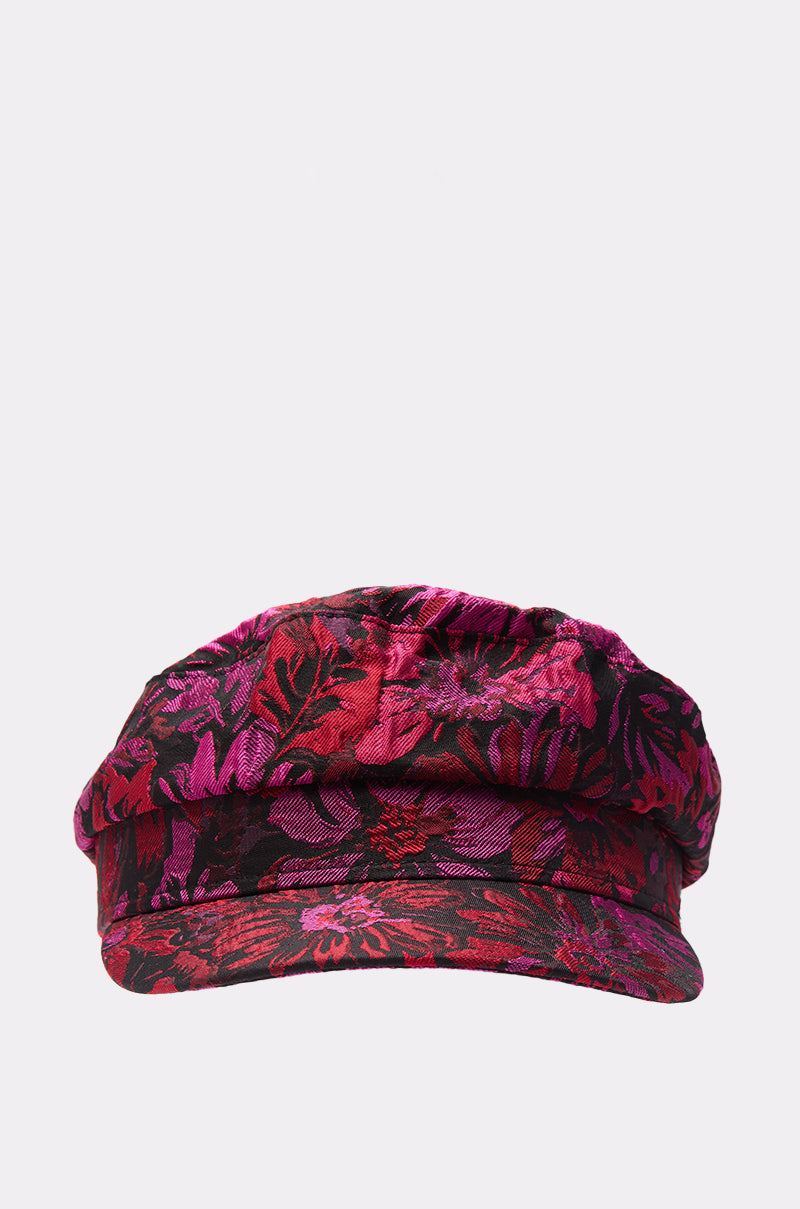 The LUXE LIVING BRIM HAT showcases a cadet-style silhouette with a bold red and pink floral brocade pattern, presented front-facing against a plain light background. 1