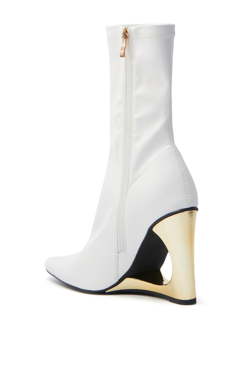 The AZALEA WANG BRIXHAM bootie features a sleek, modern design with a stylish white vegan leather body, pointed toe, and a distinctively sculpted metallic gold wedge heel with a side zipper.