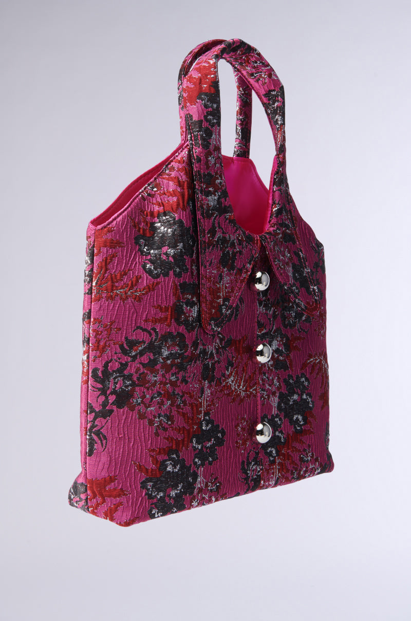 The DONT BE JEALOUS JACKET BAG features a pink brocade floral pattern with black and red designs, silver metallic accents, dual handles, a buttoned shirt collar-style AKIRA Label front, and a bright pink interior lining.