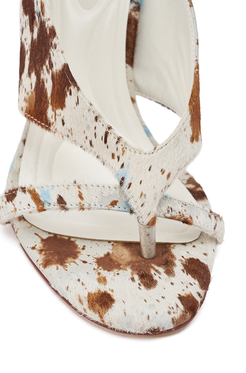 The AKIRA GOLD BRONNIE COW CHUNKY THONG SANDAL features a chunky silhouette with a white and brown cowhide pattern, western-inspired open toe design, and genuine calf hair for a textured, fur-like feel on the straps and footbed. 8