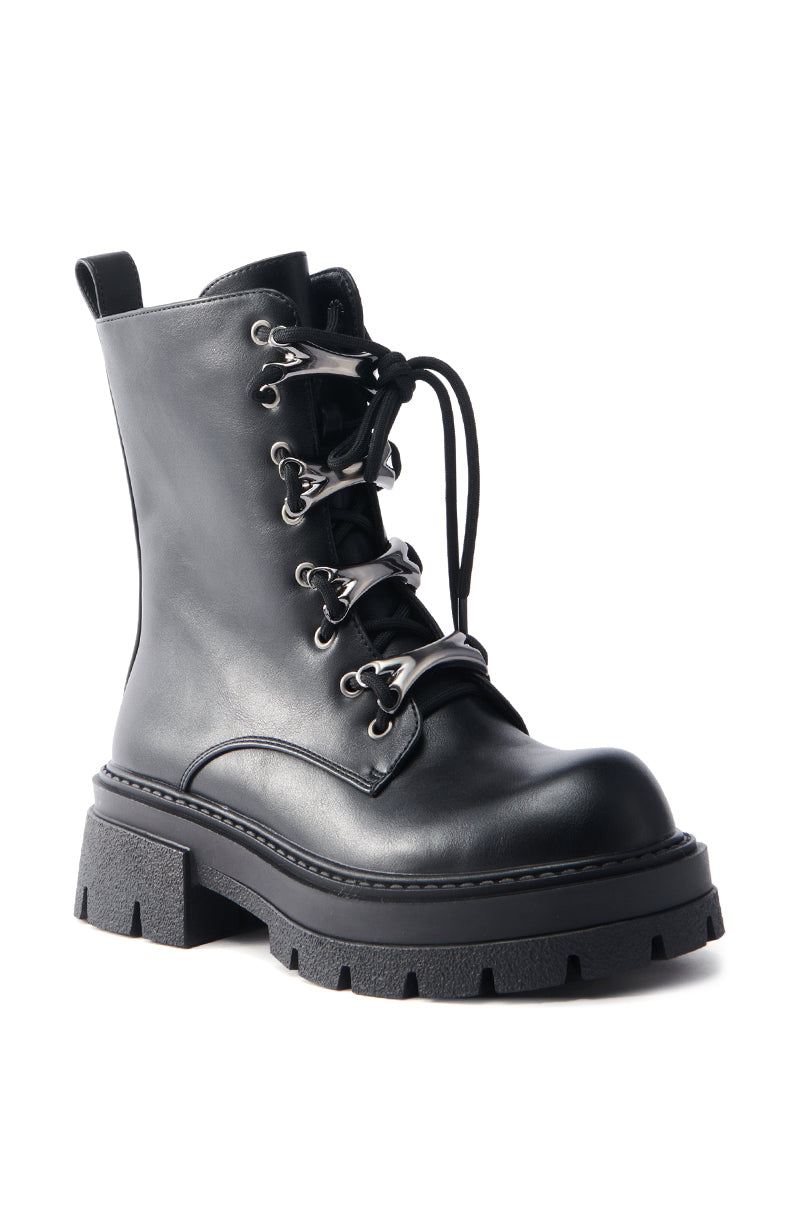 The AZALEA WANG BROOKS BLACK COMBAT BOOTIE is a black faux leather bootie with a chunky heel, metal eyelets, lace-up front, and pull tab at the heel. It showcases a rugged design and sturdy construction.