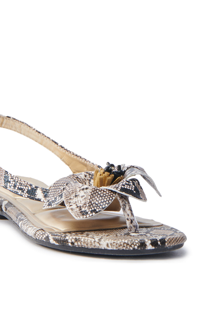 The AKIRA BRUNA SNAKE SANDAL features chic sandals with a glossy faux snakeskin pattern, a toe loop adorned with a decorative layered flower on the strap, an adjustable buckled ankle strap, and a cushioned sole for comfort.