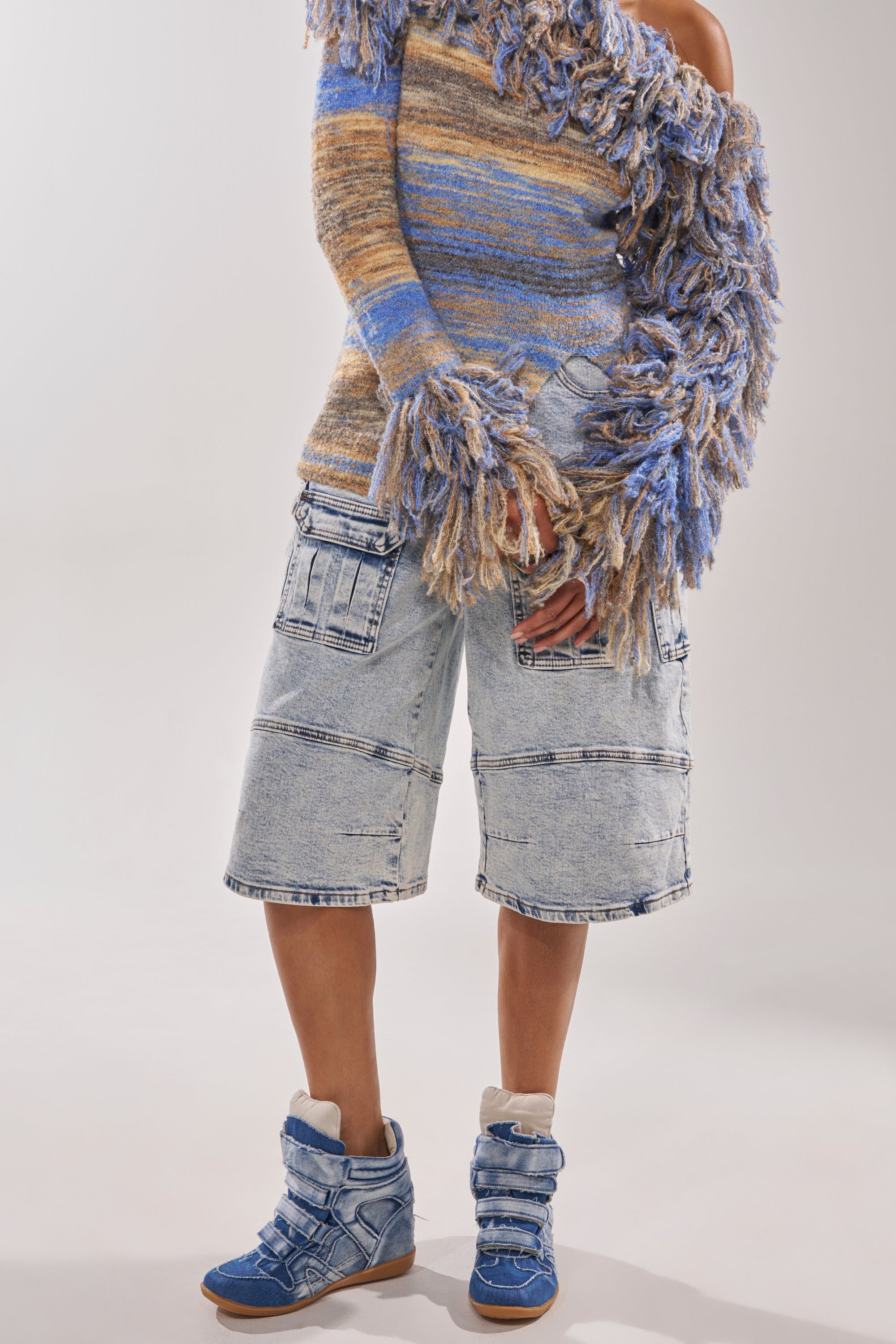 Someone wears a multicolored, textured off-the-shoulder sweater with long fringed sleeves, light denim knee-length shorts with large pockets, and AZALEA WANG BRYANT DENIM WEDGE SNEAKER in blue with white accents. 2