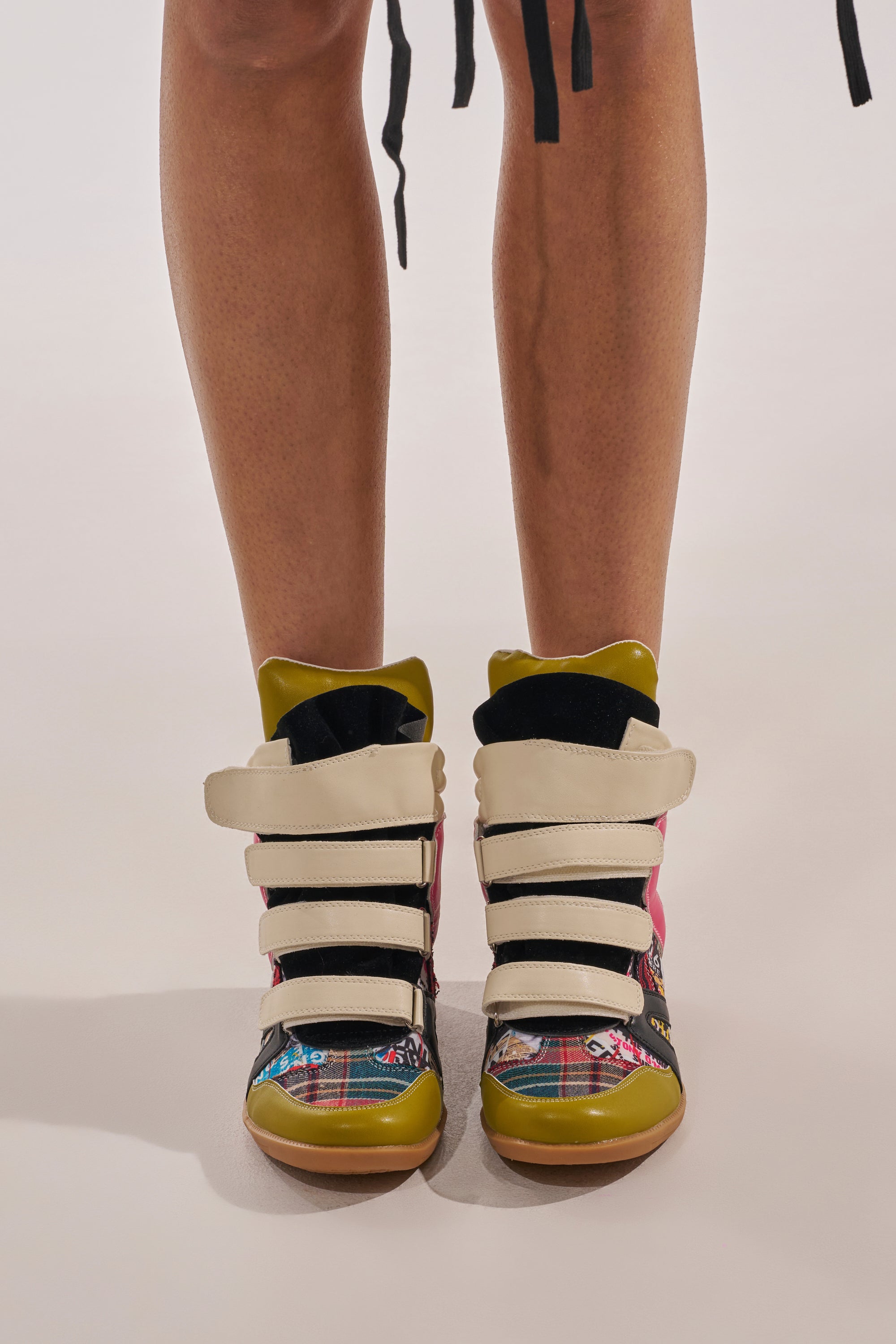 A person wears the AZALEA WANG BRYANT MULTI WEDGE SNEAKER—colorful high-tops with graphic green, pink, beige, and black straps, plus patterned panels—shown from knees down against a plain backdrop. 2