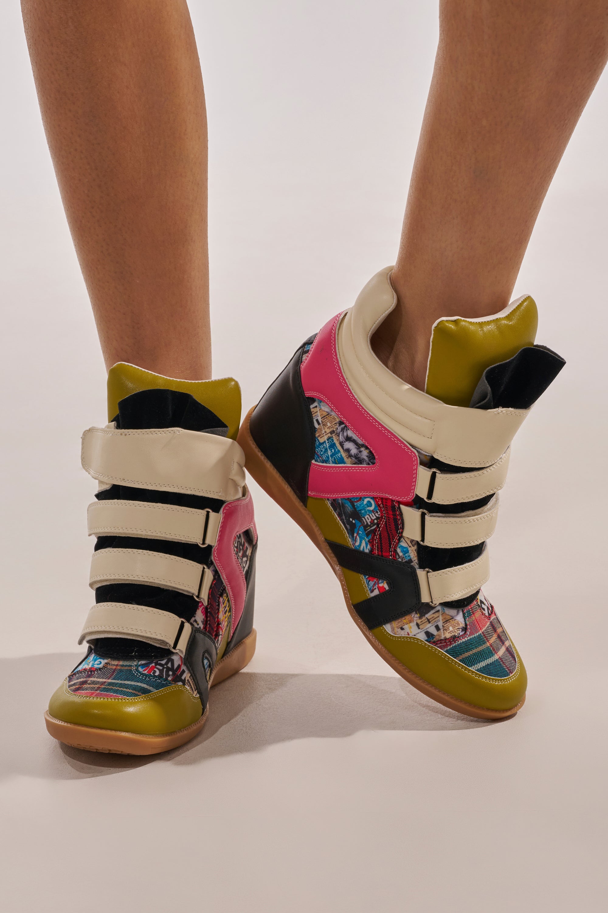 Someone wears the AZALEA WANG BRYANT MULTI WEDGE SNEAKER—faux leather high tops with velcro straps in pink, yellow, black, beige, and multicolored prints—making a bold street style statement against a plain light background. 3