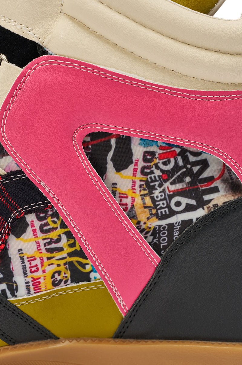 Close-up of the AZALEA WANG BRYANT MULTI WEDGE SNEAKER featuring fashion-forward, colorful leather panels in pink, cream, olive, and black with visible stitching and collage-style text and graphics under the outer layer. 9