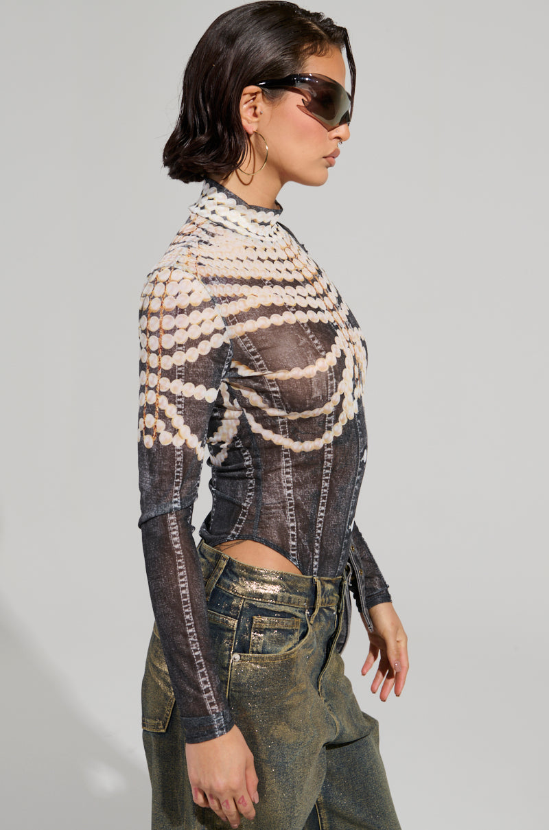 A person exudes an edgy vibe wearing dark sunglasses, the LOCKED IN BODYSUIT featuring pearl-like patterns, and metallic green pants. Their hair is styled short as they confidently walk against a plain background, rocking a sheer mesh look that adds an unexpected twist to their ensemble.