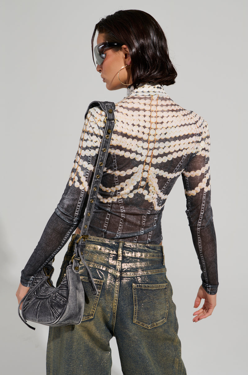 A person with shoulder-length dark hair wearing sunglasses, styled in the LOCKED IN BODYSUIT resembling sheer mesh and draped pearls, paired with metallic jeans that mimic faux denim, holds a gray purse. Standing against a light gray background, the person poses with their back to the camera.