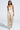 A woman in a LOTS OF LOVE SATIN PALAZZO PANT with abstract print, beige and white hues, walks gracefully and confidently. Her long hair flows past hoop earrings, paired with platform sandals. The high-rise fit adds elegance against the plain, light-colored background.