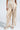 Wearing the LOTS OF LOVE SATIN PALAZZO PANT, the person exudes confidence in high-rise, beige and white wide-leg pants with a drawstring waist. Open-toed platform sandals complete the look against a light gray backdrop, enhancing their elegance.