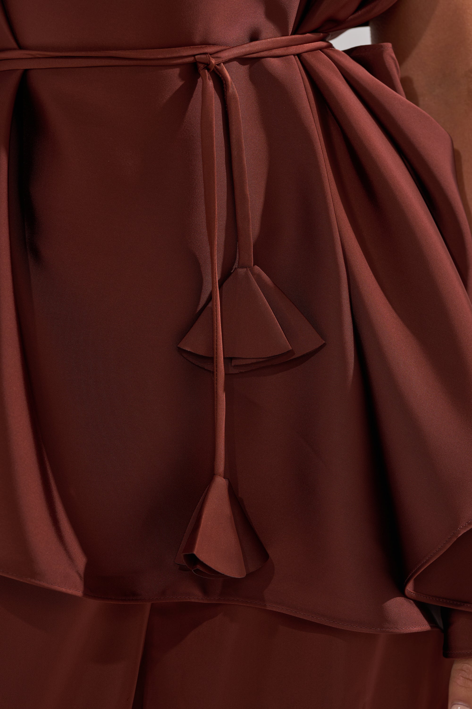 Close-up of a person wearing the HIGH SOCIETY BLOUSE in rich brown satin, featuring layered fabric and a thin waist tie with geometric tassel ends for a textured, elegant look.