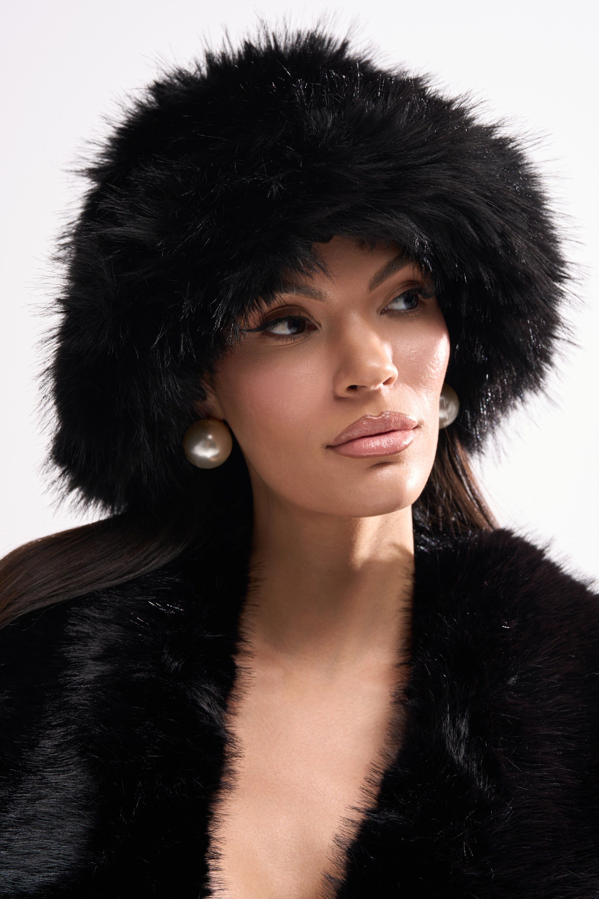 A woman models the CHIC FAUX FUR BUCKET HAT in black, styled with a matching faux fur coat and bold pearl earrings, as she gazes to the side against a simple light backdrop. 0