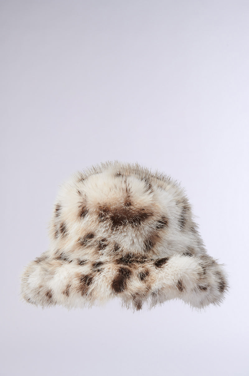 The LEO BABE FAUX FUR BUCKET HAT boasts a fluffy design with a cheetah print pattern on a plain background. Its oversized brim is richly adorned in shades of brown and beige, showcasing distinctive spotted patterns. 1