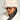 Wearing a stylish accessory ensemble, the person sports the TOASTIE FAUX FUR BUCKET HAT in beige alongside a cozy faux fur coat, paired perfectly with oversized round sunglasses and hoop earrings. Their long, dark hair falls gracefully against the simple background.