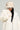 A person wearing a plush white coat and the trendy TOASTIE FAUX FUR BUCKET HAT, with long dark hair cascading from underneath. They're accessorized with sunglasses and large hoop earrings, standing against a neutral background. Their expression radiates confidence and style.