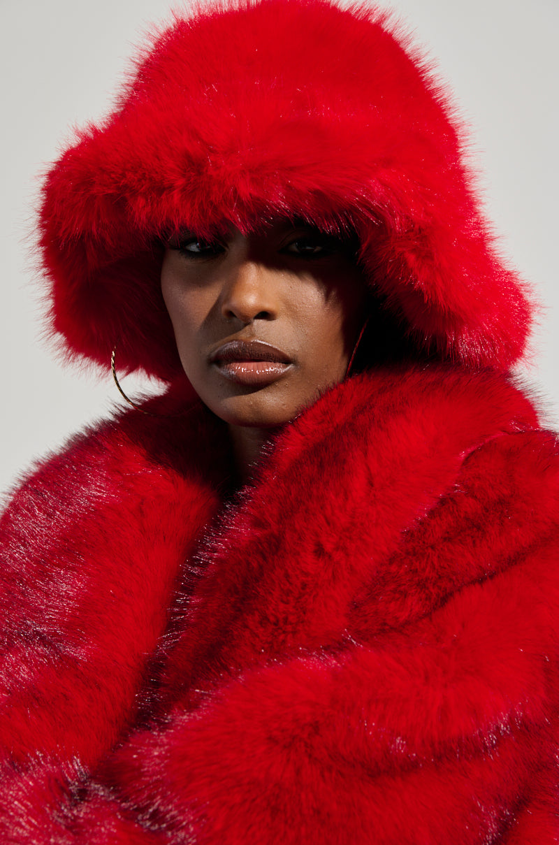 Draped in a luxurious oversized red fur coat, a person wearing the LOOK AT ME NOW FAUX FUR HAT exudes confidence, with large hoop earrings adding flair. The neutral background enhances this vibrant ensemble, making it an ideal accessory for cold weather. 1