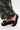 A close-up of a person wearing BUDZA BLACK FLATFORM SANDALS with an open almond toe, paired with green patterned wide-leg pants, standing on a light-colored surface.
