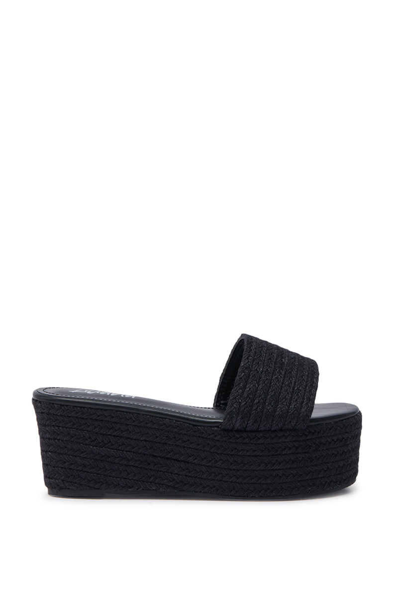 The BUDZA BLACK FLATFORM SANDAL features a woven-look black rattan wide strap, flatform sole, and open almond toe for a modern, comfortable style.
