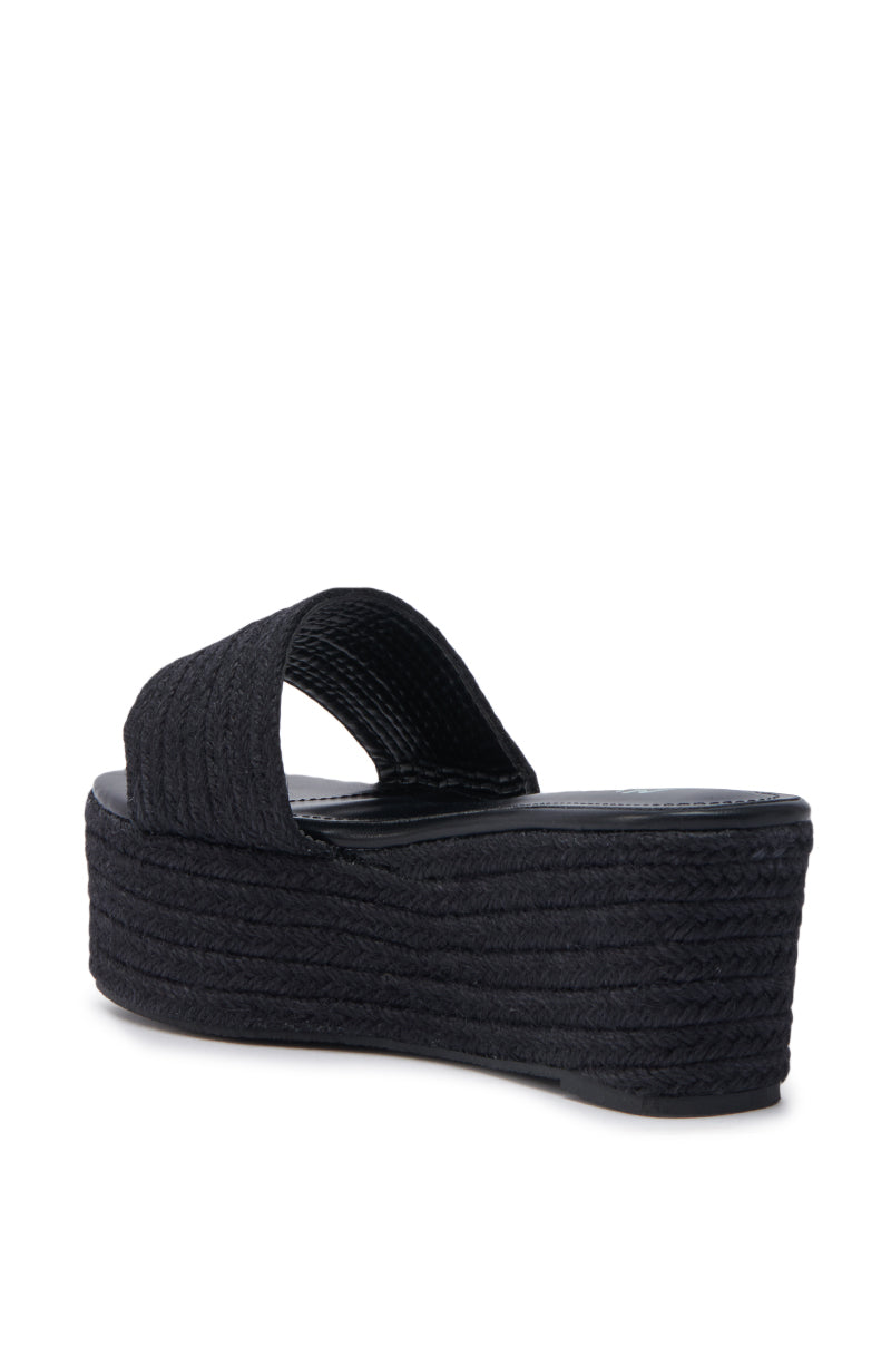 The BUDZA BLACK FLATFORM SANDAL, shown from the back and slightly to the side on a white background, features black rattan material, an open almond toe, a wide textured strap, and a thick flatform sole.