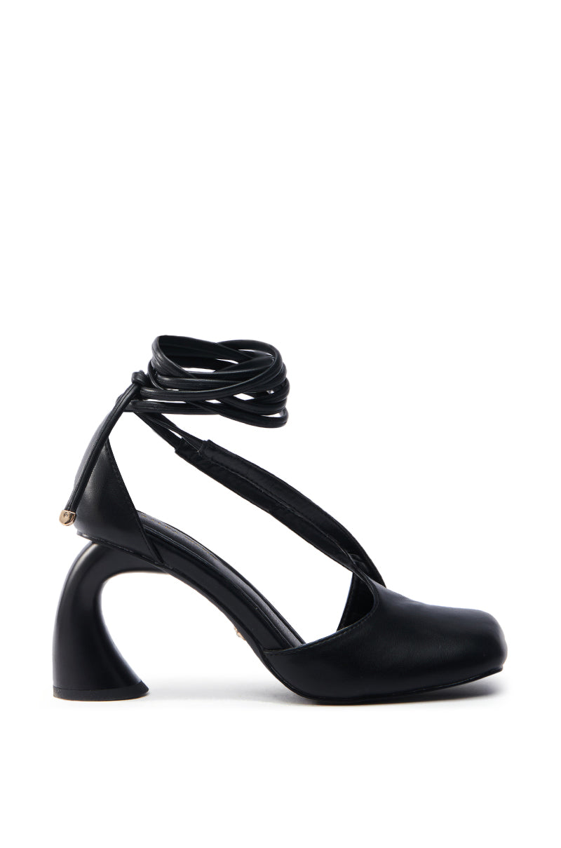 Introducing the AZALEA WANG BUIKY BLACK PUMP: a sleek black high-heeled shoe made from faux leather, featuring a unique sculpted heel and wrap-around ankle straps. This closed-toe design effortlessly combines elegance with the minimalist balletcore trend.