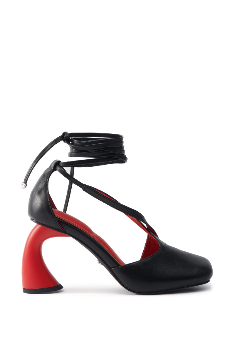 The AZALEA WANG BUIKY BLACK AND RED PUMP showcases faux leather, a chunky sculptural red heel, ankle wrap straps, and a red interior accent, elegantly displayed on a white background.
