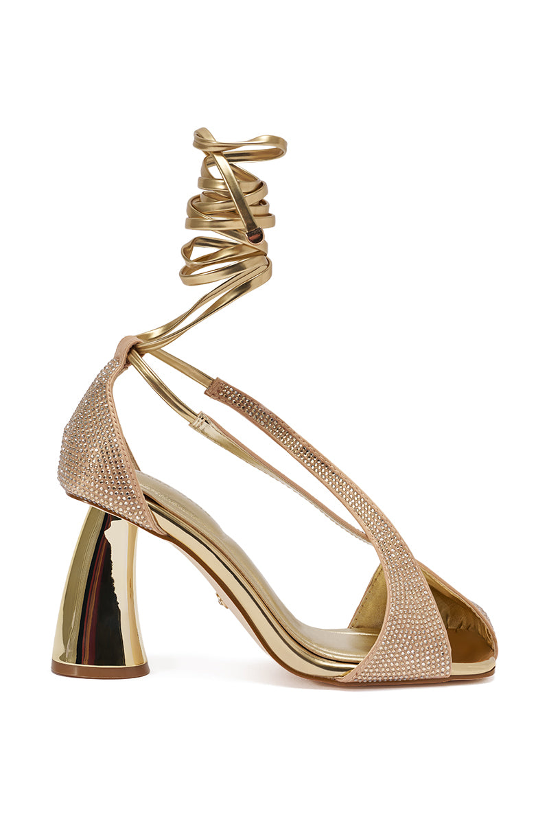 The AZALEA WANG BUILANY GOLD RHINESTONE CHUNKY PUMP is a gold open-toe high-heeled sandal featuring sparkling rhinestones, a chunky metallic gold heel, ankle wrap straps, and a cushioned insole for extra comfort.