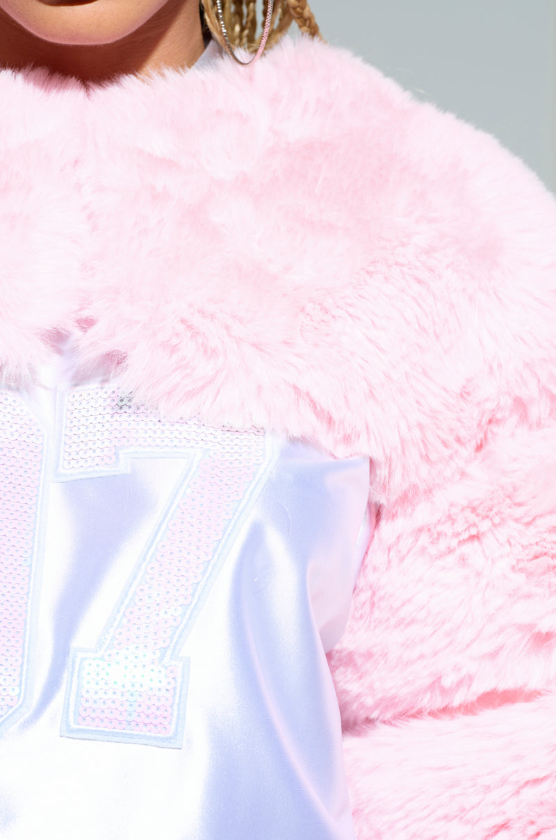 Close-up of a person wearing the LADIES NIGHT FAUX FUR BOLERO in a fluffy pink shade, paired with a white satin top featuring sparkly letters "17." The soft, plush texture of the bolero beautifully contrasts with the silky smooth fabric of the top, making it ideal for a ladies' night out.