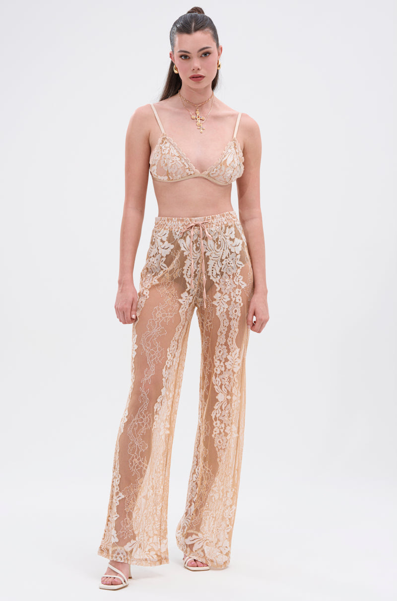 A woman with long hair pulled back wears the RESORT VIBES BRA TOP, a sheer beige floral lace bralette, paired with matching wide-leg tie-waist pants. She accessorizes with heeled sandals and gold jewelry against a plain background. 5