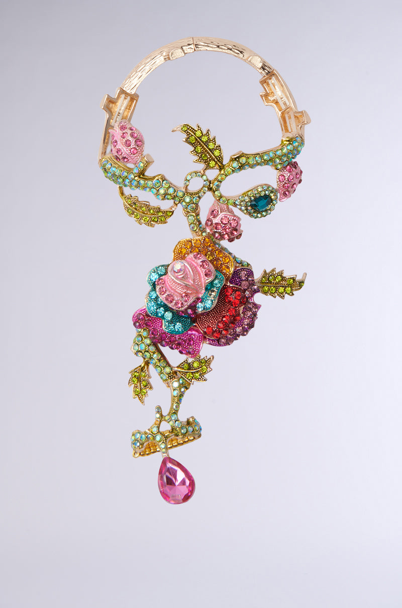 The MY SECRET GARDEN LUXE GEM BRACELET RING COMBO features a floral motif with colorful rhinestone flowers and leaves, plus a large pink teardrop gem. Reds, blues, and greens adorn its gold-toned vine-like structure.