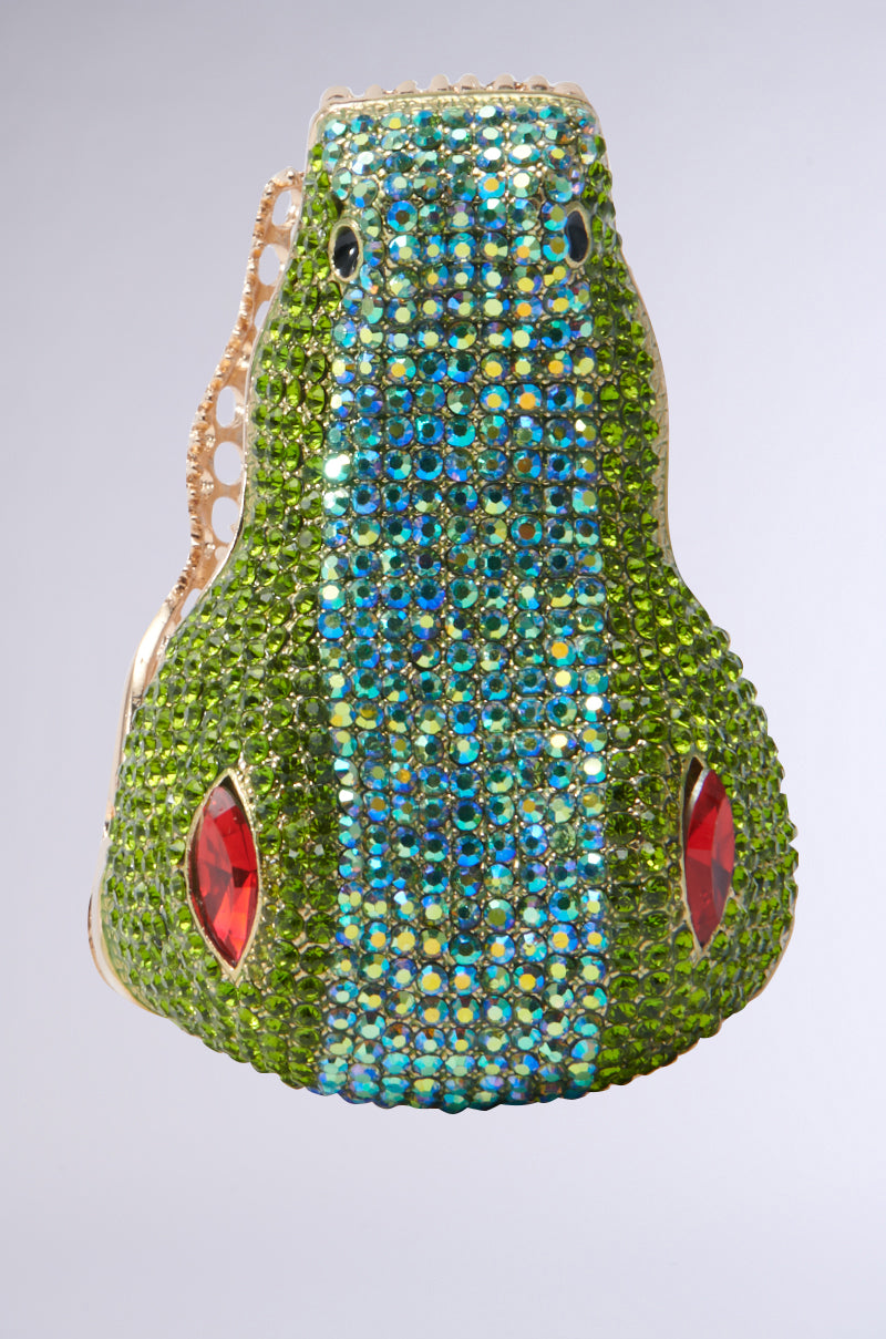 Introducing the BITE ME CUFF BRACELET: an evening accessory shimmering with multicolor rhinestones. This frog-shaped piece features blue eyes and a body that dazzles in green with red side accents, capturing the essence of a crocodile-shaped cuff on a soft gradient background. 3