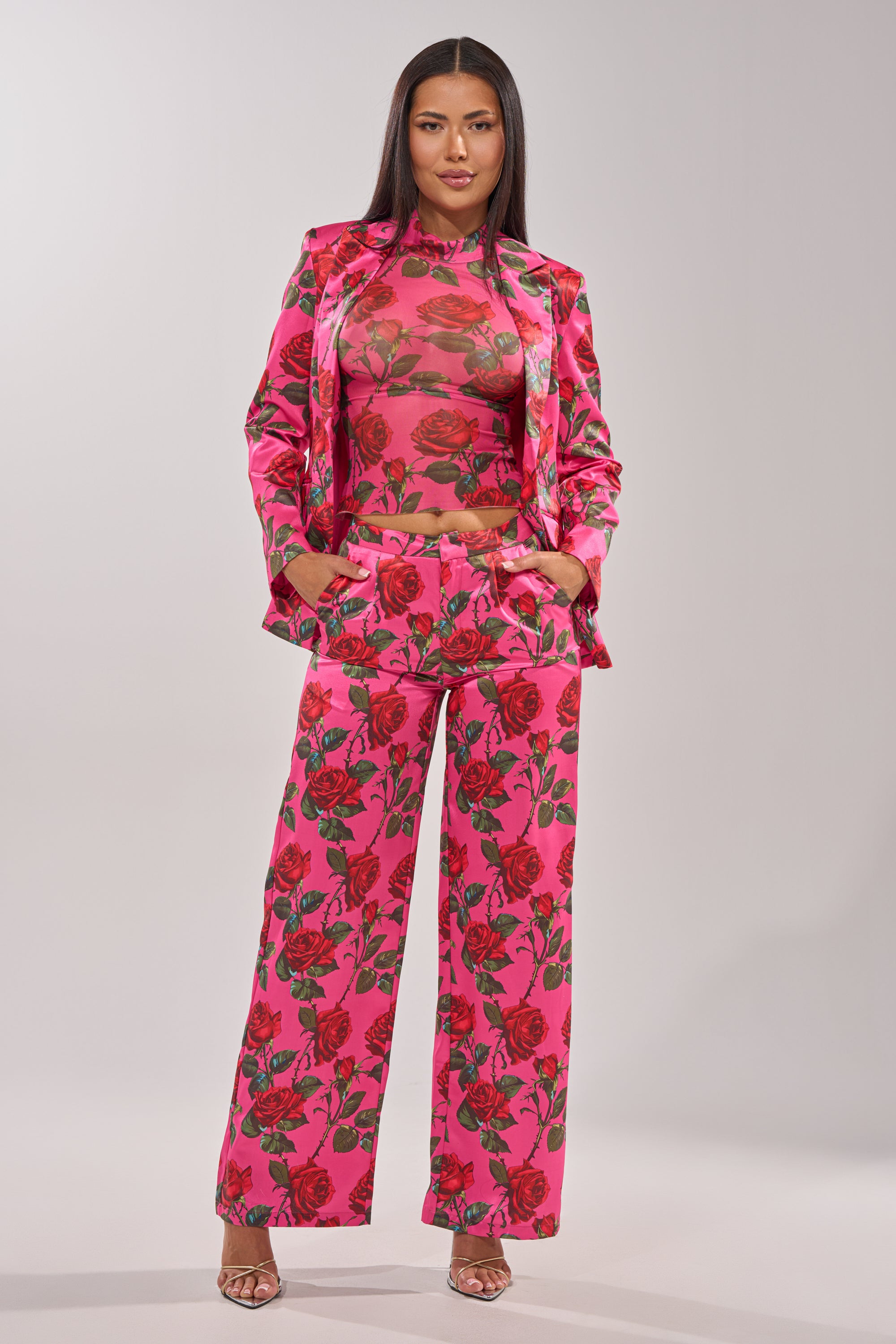 A woman poses confidently in the DOZEN ROSES SATIN PANT IN FUCHSIA, her long straight hair flowing and one hand in her pocket, set against a plain light background. 4
