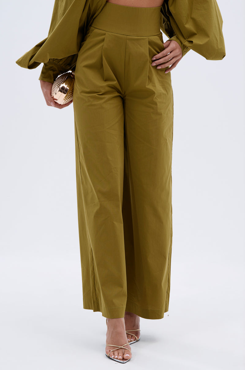 Model wears the GOLD COAST WIDE LEG PALAZZO PANT with a wide-leg silhouette, paired with a matching long-sleeve top, clear-heeled sandals, and a round gold clutch, posed against a simple light background. 1
