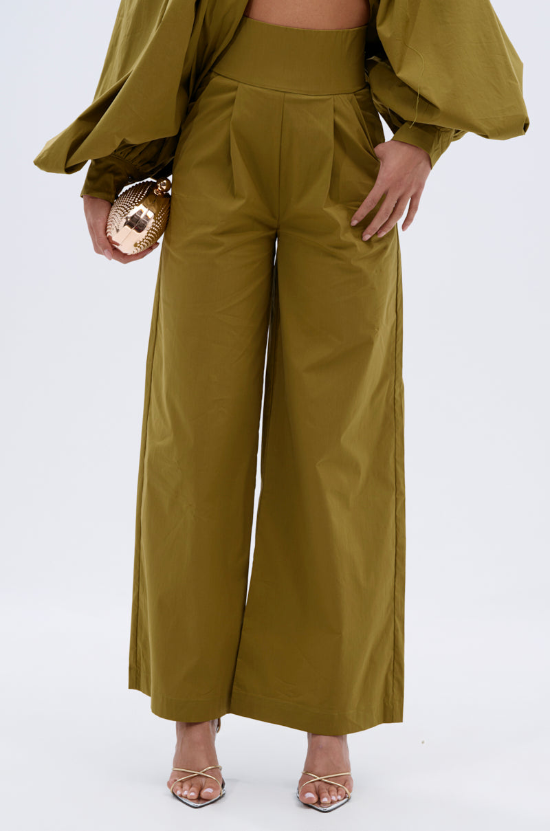 Wearing the GOLD COAST WIDE LEG PALAZZO PANT in olive green with a matching loose top, she accessorizes with a round gold clutch and strappy heels. 2