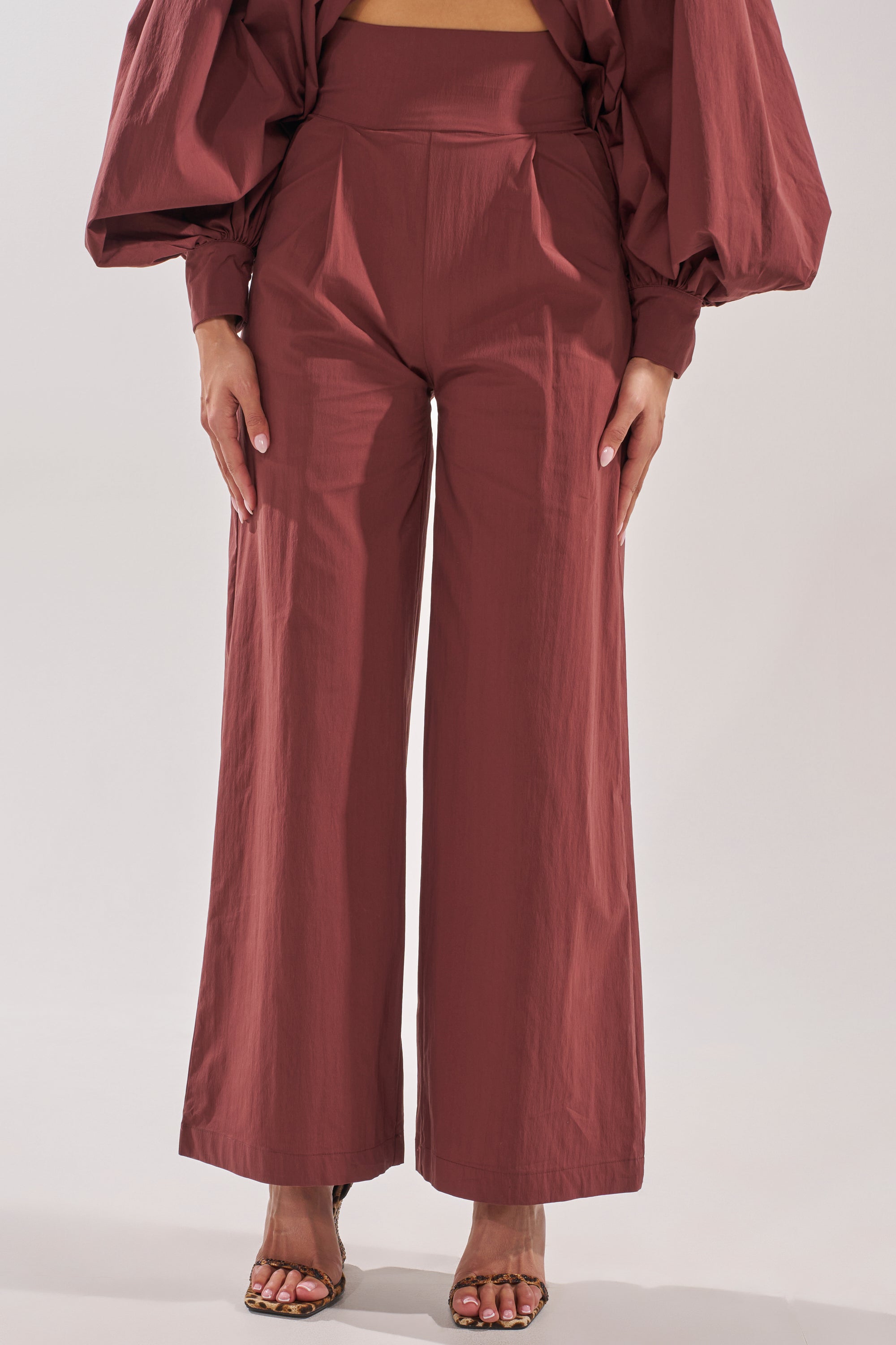 A woman wears the GOLD COAST WIDE LEG PALAZZO PANT IN BROWN with a matching voluminous-sleeve top and open-toe heeled sandals, standing against a plain background. 2