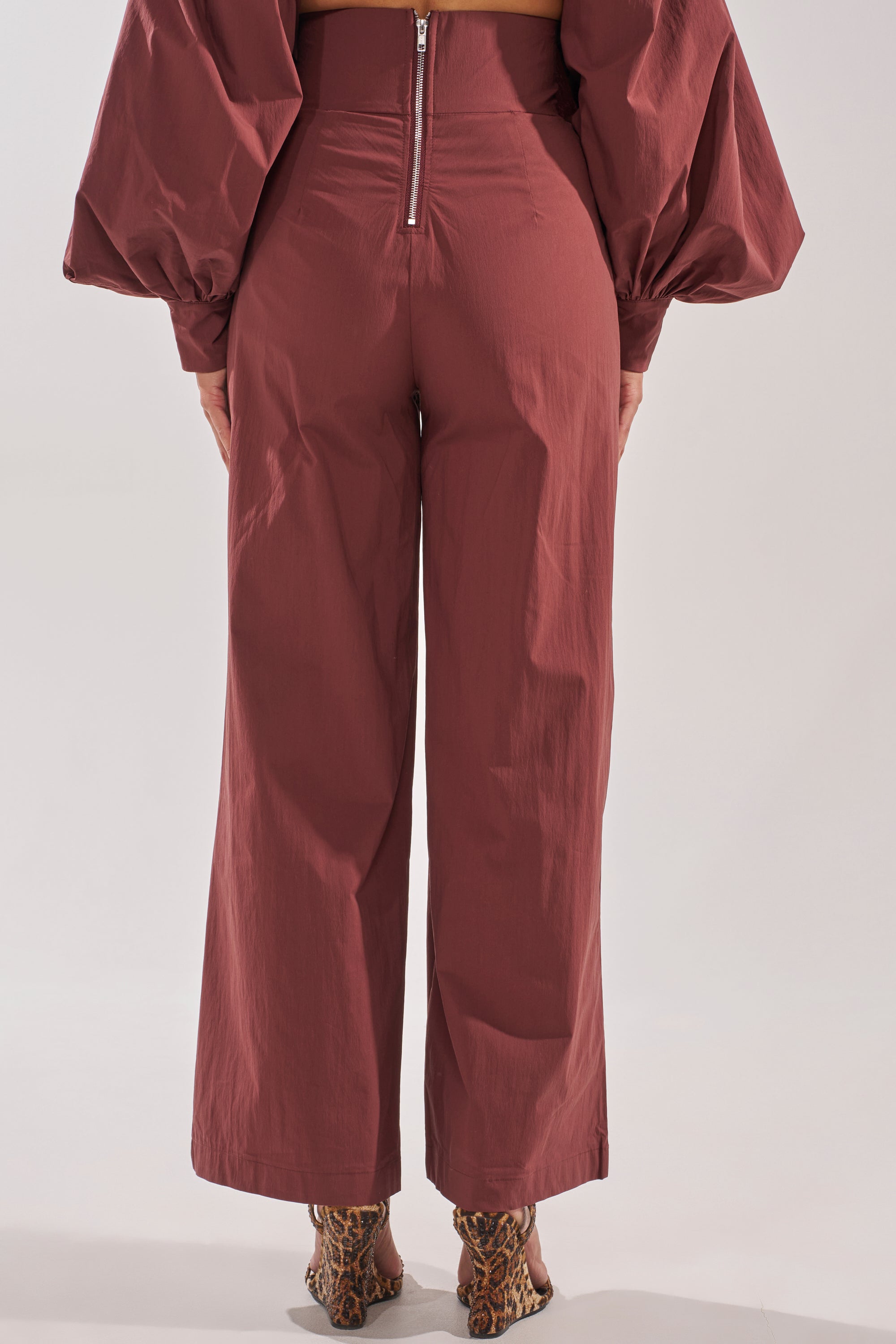 A person is shown from the back wearing the GOLD COAST Wide Leg Palazzo Pant in brown with a back zipper, paired with a matching maroon top with puffed sleeves and leopard-print heeled shoes. 4