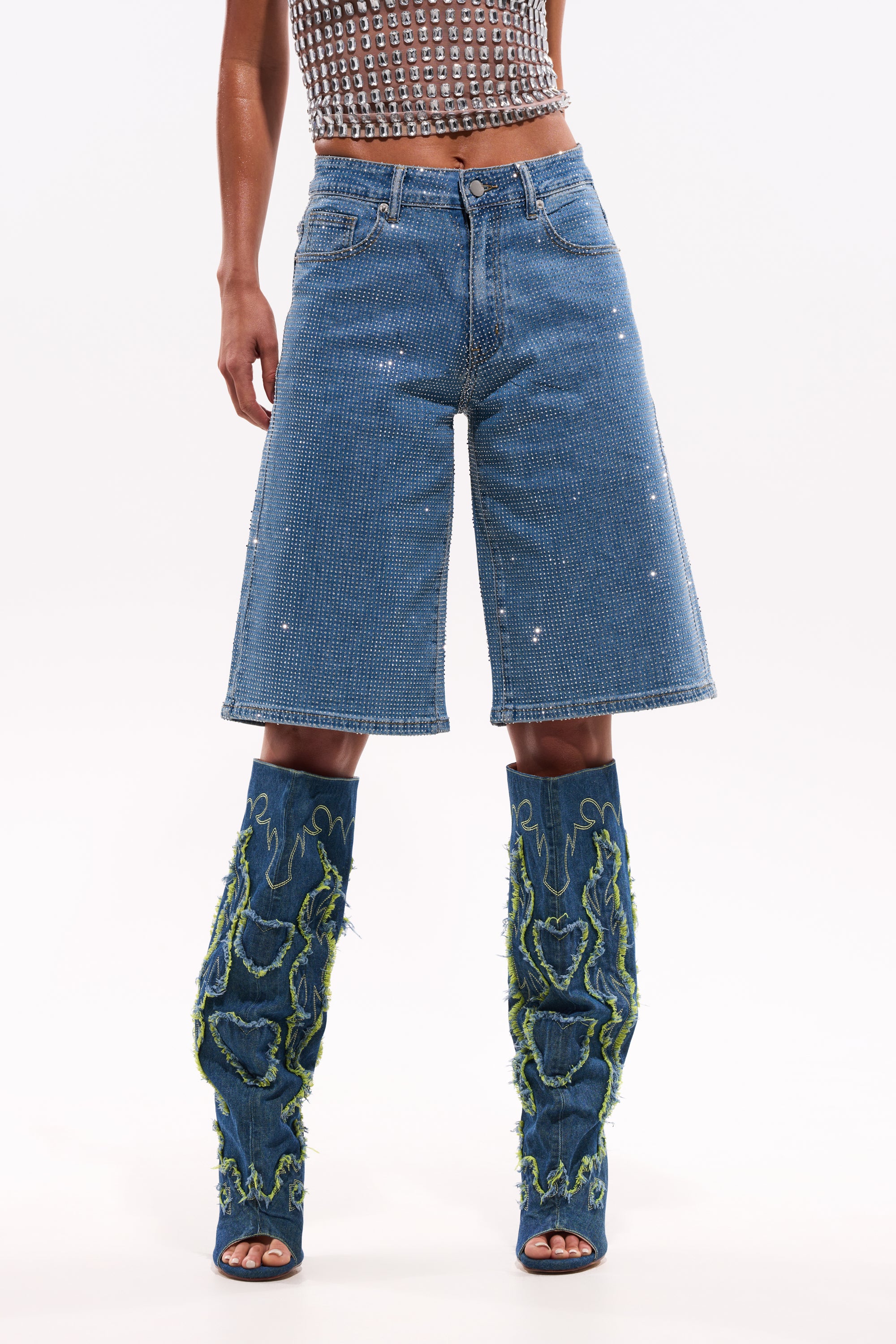 Someone wearing the BLING BLING RHINESTONE DARK BLUE DENIM BERMUDA SHORT, paired with a sleeveless patterned top and tall open-toe denim boots with green stitching and frayed details. 13