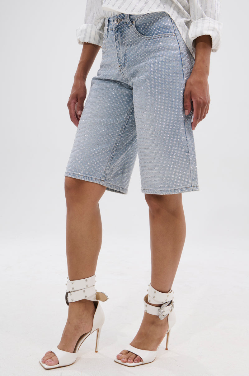 A person wearing BLING BLING RHINESTONE BERMUDA SHORTS, a white long-sleeve shirt, and white high-heeled sandals with ankle straps stands against a plain white background.