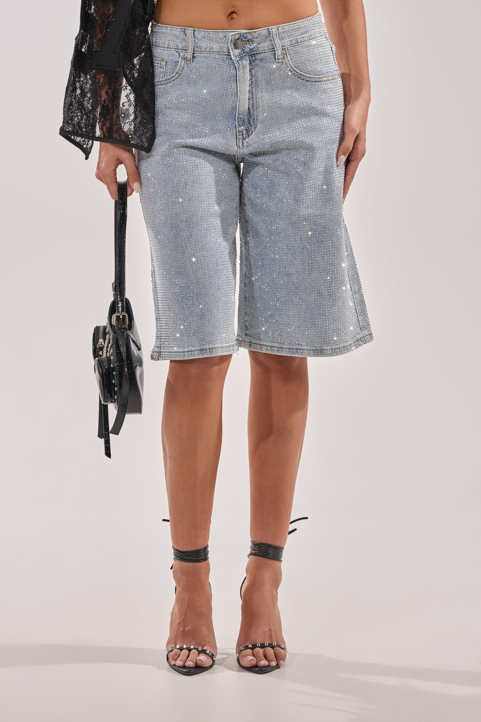 Wearing BLING BLING RHINESTONE BERMUDA SHORT IN LIGHT BLUE DENIM with black strappy high-heeled sandals and a small black handbag. 1