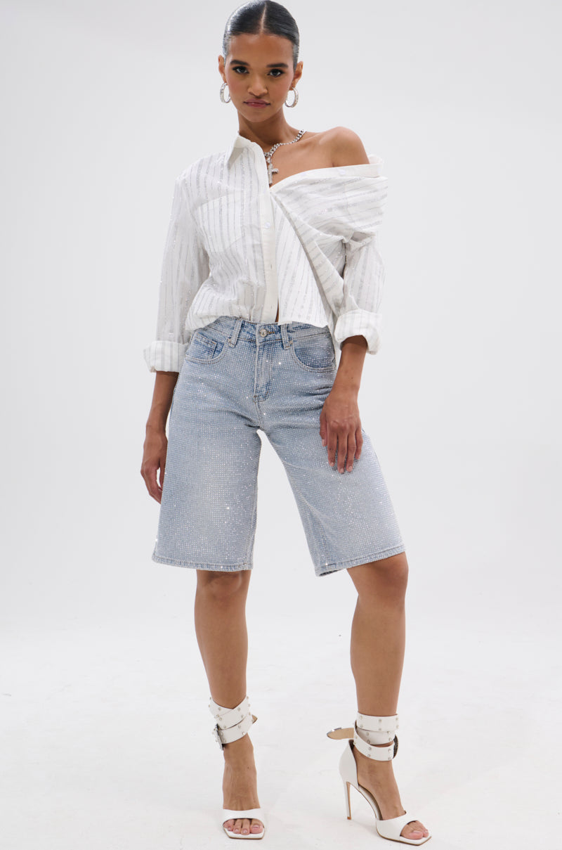 A woman poses confidently in a white off-the-shoulder striped blouse, BLING BLING RHINESTONE BERMUDA SHORT, white high-heeled sandals, and hoop earrings against a plain white background.
