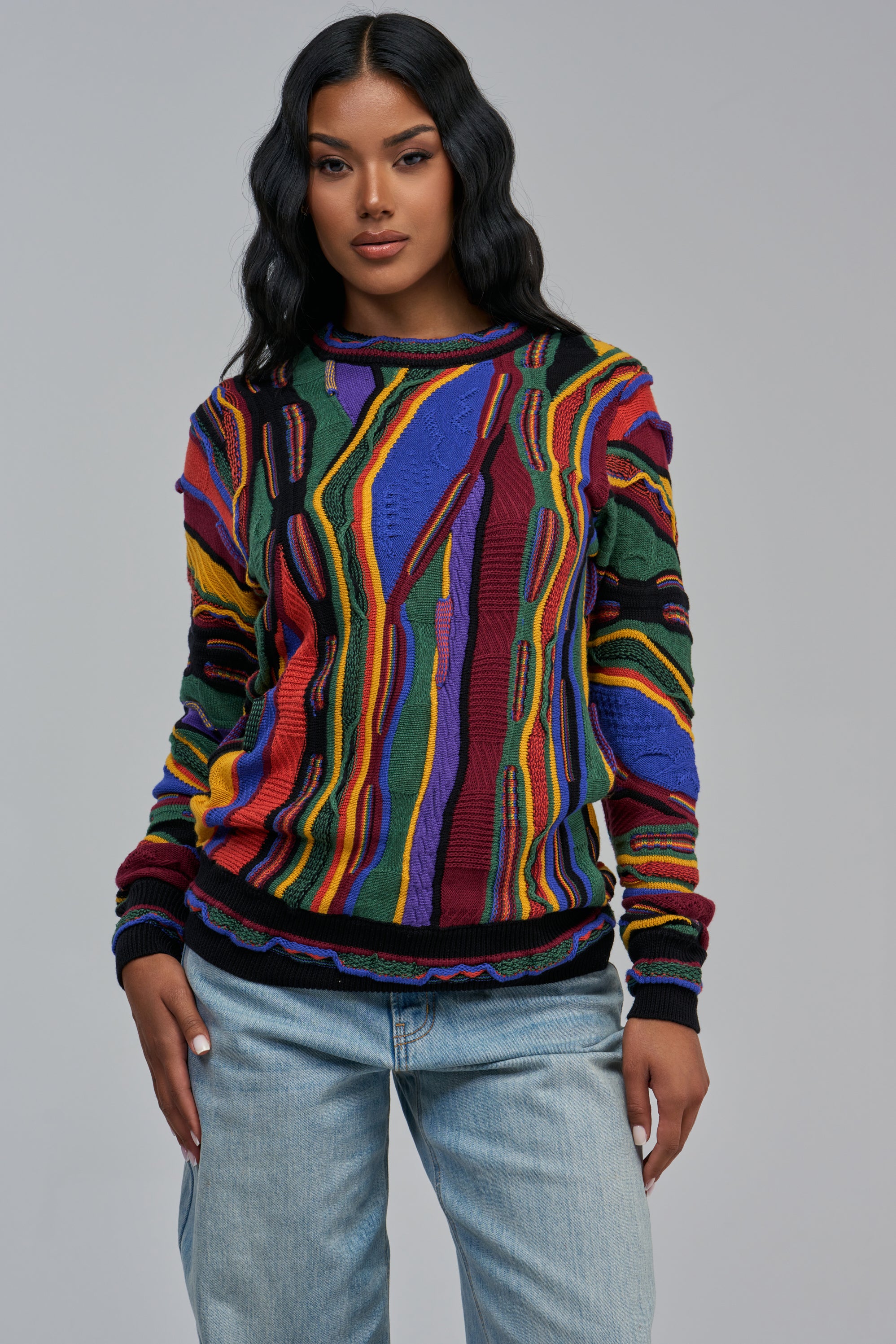 A person wearing a VINTAGE OVERSIZED SWEATER IN BLUE MULTI with an oversized retro abstract, textured pattern and light-wash denim jeans.