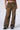 The model is showcasing the MIMI CHEETAH PANT, a pair of mid-rise brown leopard-print wide-leg pants featuring extensive ripped and frayed details down the front of both legs. These pants have a relaxed fit, complemented by black chunky shoes worn by the model.