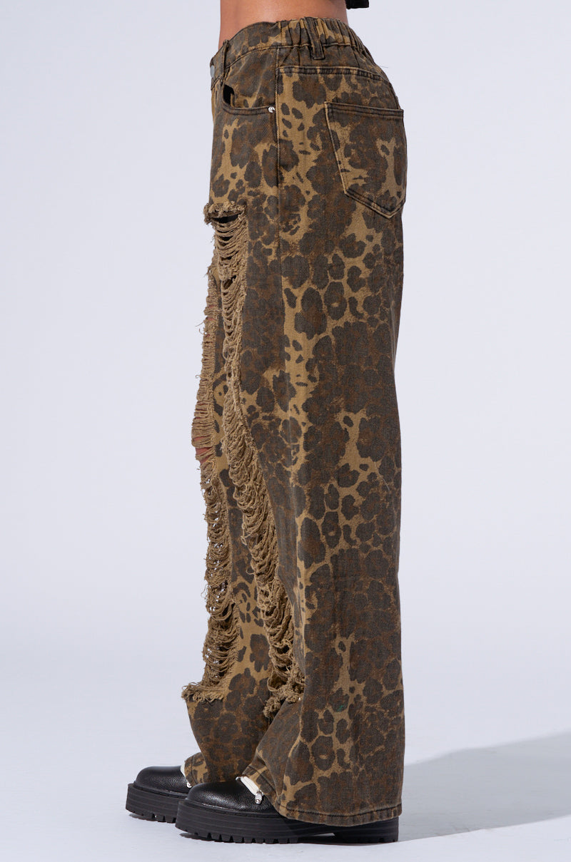 Side view of the MIMI CHEETAH PANT, featuring a brown cheetah print with extensive ripped detailing along the outer seam from the thigh down to the ankle. These mid-rise pants have a straight-leg cut, and they are paired with black chunky shoes. Only the pants and shoes are visible. 4