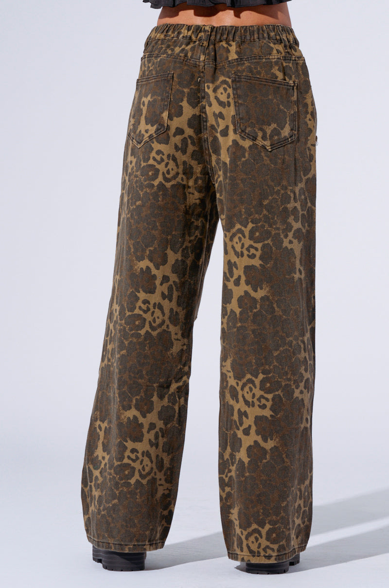 A person is wearing the MIMI CHEETAH PANT, featuring a high-waisted, loose-fitting design with a cheetah print in brown and black. The pants include two back pockets and are paired with black shoes. The person's upper body is not visible. 5