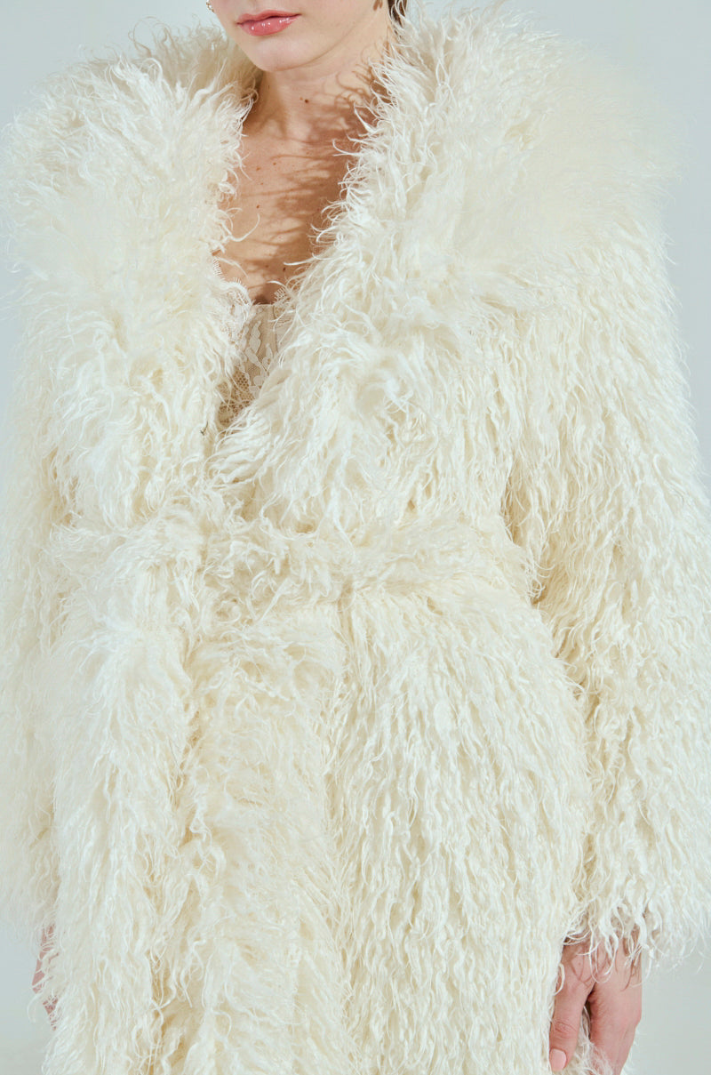 The person, with only their lower face and upper body visible, wears the SNOW WHITE TRENCH - a fluffy, white faux fur coat with long, soft fibers and a wide collar that captures an enchanting allure.