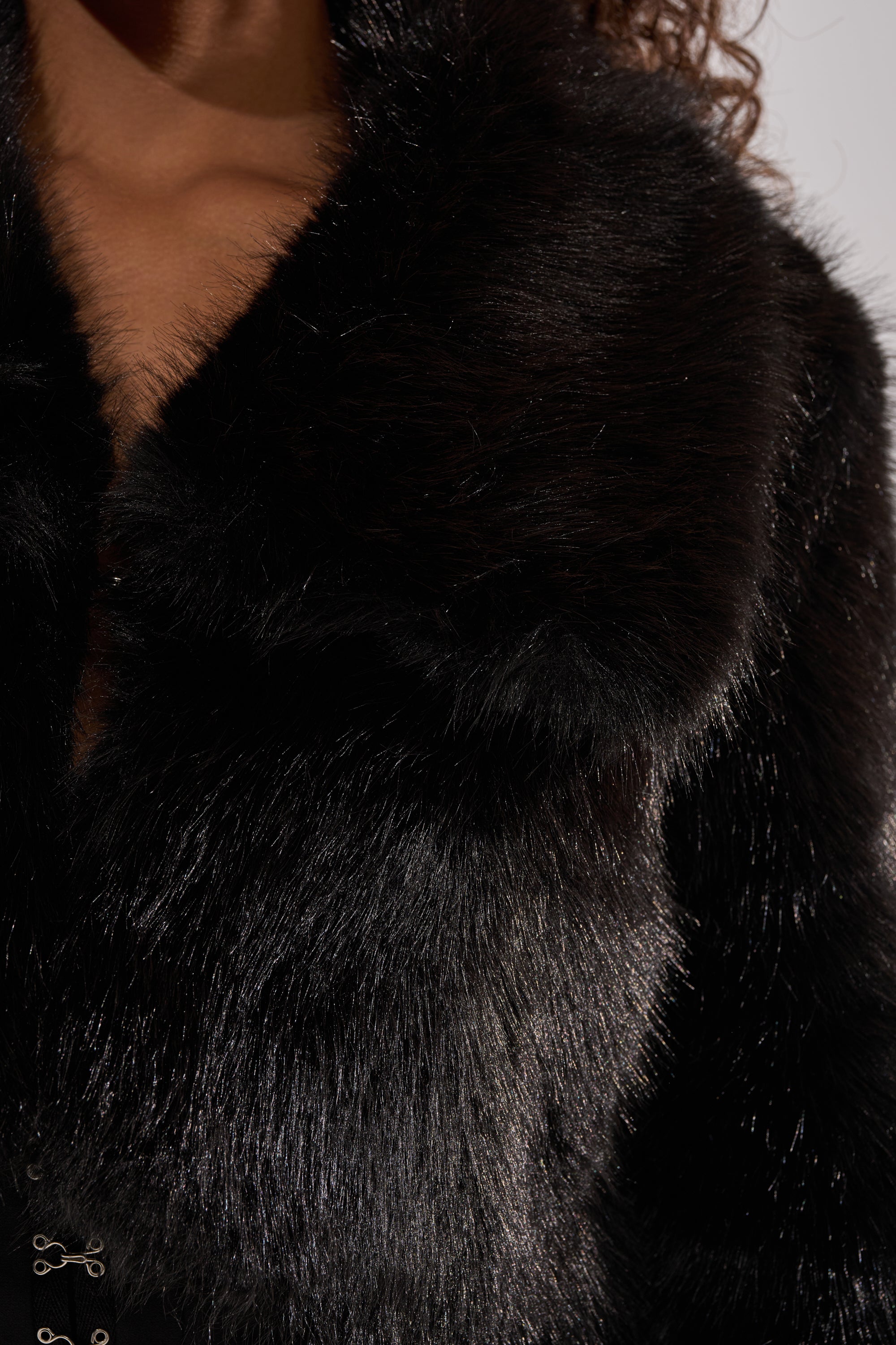 Close-up of a person wearing the CADENCE FAUX FUR IN BLACK, showcasing its luxurious texture and glossy finish. Part of the person's neck and curly hair appears at the top left, highlighting the elegance of the faux fur.