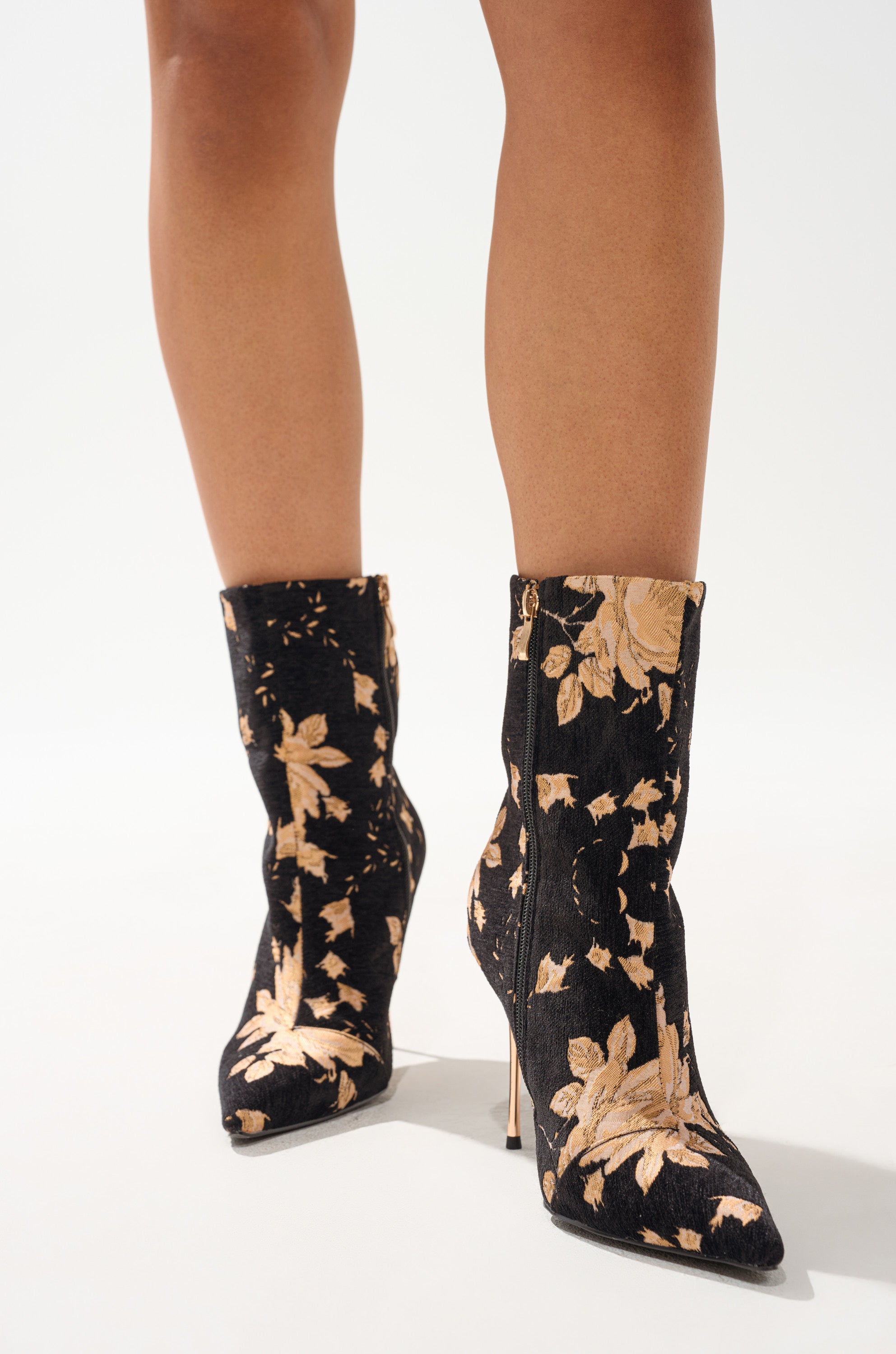 A person wearing AZALEA WANG CALEAN BLACK MULTI BROCADE STILETTO BOOTIES with a gold floral pattern and pointed toes stands on a white background. 1